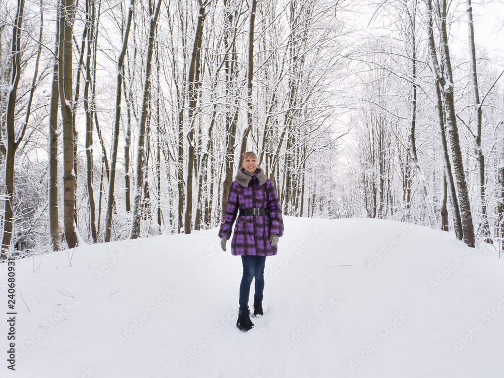 A beautiful slender young woman rejoices in a snowy park.