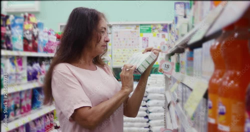 Side view of adult woman reading information on package of product while shopping on market Side view of adult woman reading information on package of product while shopping on market