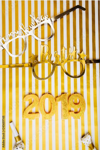 New Years Eve celebration background , 2019 number made with golden glitter canles, flatlay over a striped golden white board, luxury holiday concept, with funny parts glasses.