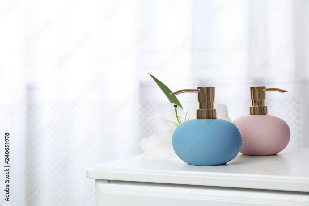 Stylish soap dispensers and lily on table against blurred background. Space for text Stylish soap dispensers and lily on table against blurred background. Space for text