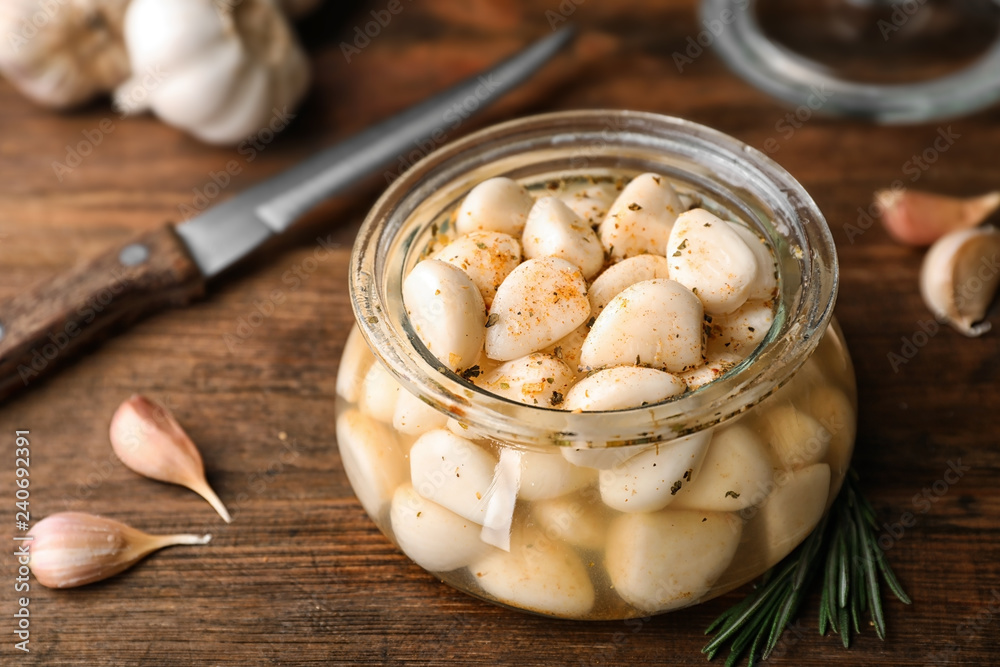 Preserved garlic in glass jar on wooden table, closeup Preserved garlic in glass jar on wooden table, closeup