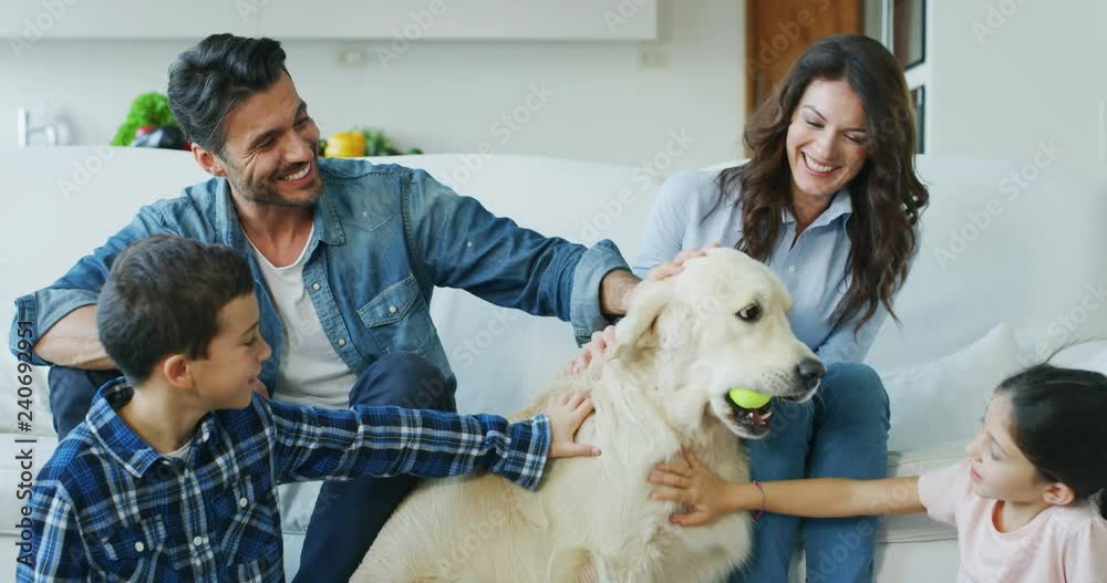 Portrait of happy family cuddling their dog having fun together in living room in slow motion. Shot with RED camera in 8K. Concept of happy family, parenthood, love for animals