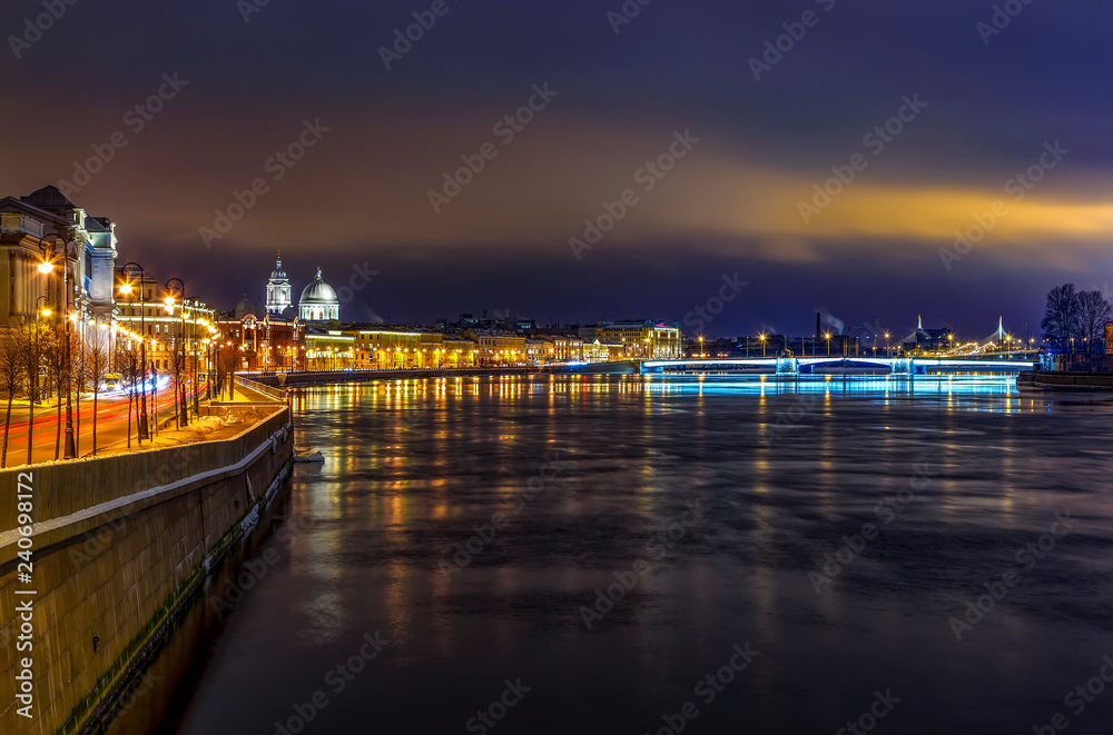 Neva river embankment with historical buildings on the shore and reflection of night lights in water, beautiful sunset sky. Petersburg, Russia