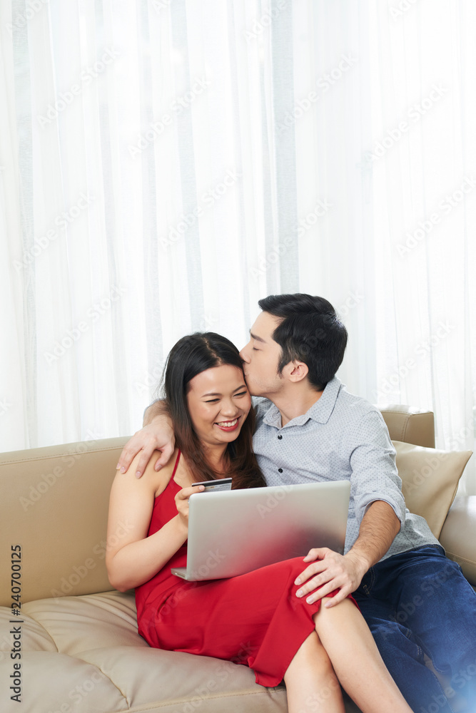 Young mixed-race couple in love shopping online for Valentine s Day presents and kissing Young mixed-race couple in love shopping online for Valentine s Day presents and kissing