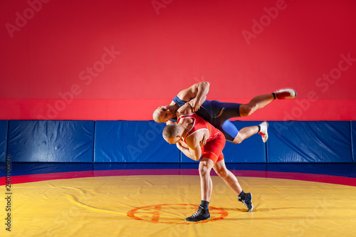 Two greco-roman  wrestlers in red and blue uniform wrestling   on a yellow wrestling carpet in the gym. The concept of fair wrestling © Виталий Сова