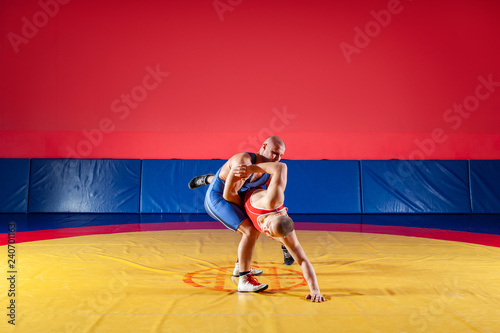The concept of fair wrestling. Two young men in blue and red wrestling tights are wrestlng and making a hip throw on a yellow wrestling carpet in the gym © Виталий Сова