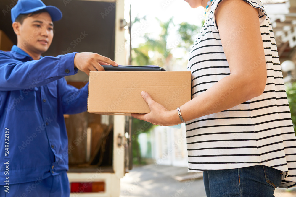 Woman taking parcel and tablet computer to sign for delivery Woman taking parcel and tablet computer to sign for delivery