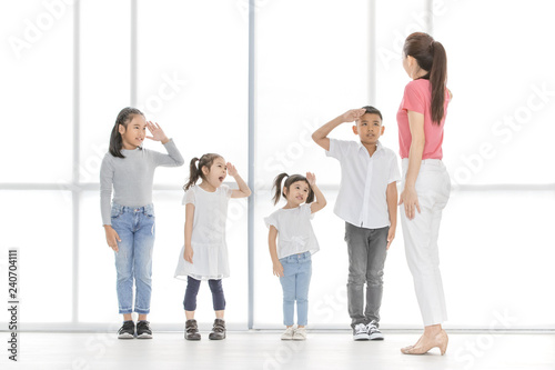 Asian kids salute to Asian woman in pink shirt, she salute backto them, they stand in front of big white window. photo