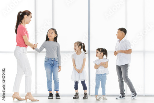 Asian woman in pink shirt teach Asian boy and girls to move their body, they stand in front of big white window.