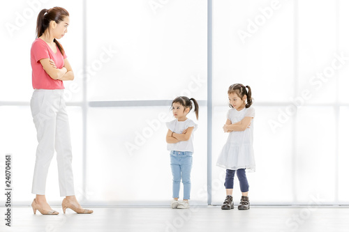 Asian woman in pink shirt and Asian boy and girls cross their one's arm, they stand in front of big white window.