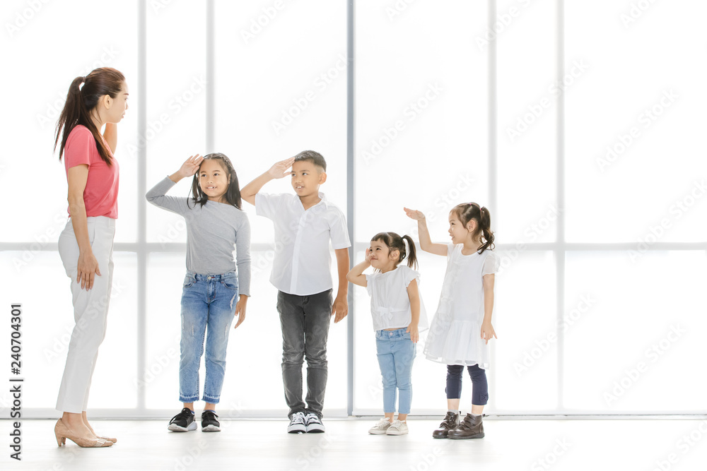 Asian woman and little Asian boy raise their one's hand among Asian kids in front of big white window.