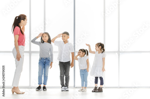 Asian woman and little Asian boy raise their one s hand among Asian kids in front of big white window.
