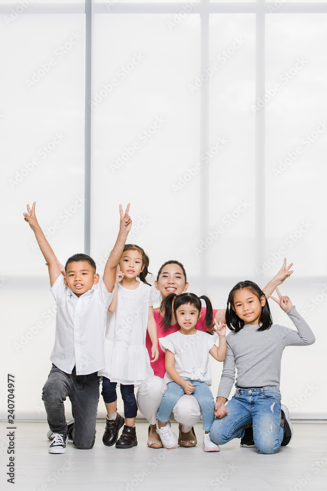 Fototapeta premium Smile Asian woman in pink shirt and Asian boy and girls squat on floor together, big white window behind them.