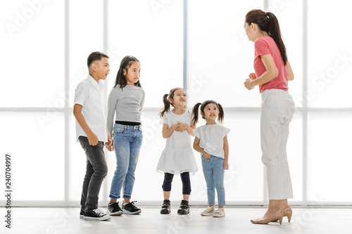 Asian woman in pink shirt teach Asian girls and boy some acting to act fake cry, they stand in front of big white window.