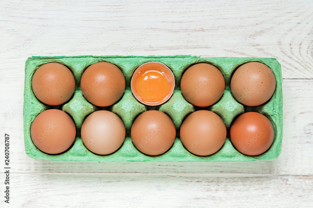 top view of green carton egg box full of raw fresh brown chicken eggs and egg yolk on wooden background top view of green carton egg box full of raw fresh brown chicken eggs and egg yolk on wooden background