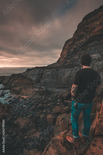Man looking at sunset and cliffs with rocks