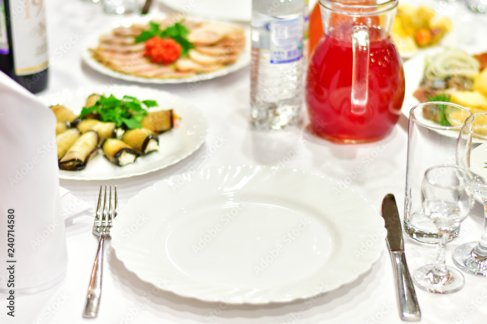 details of serving tables for a banquet in a restaurant. grapes, kiwi, tangerines, deli meats, white plates and white napkins. wine glass and vodka glasses on the table. selective focus