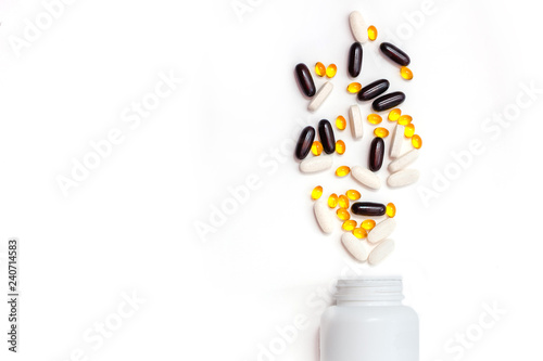 scattered tablets of vitamins spilling from white bottle with copy space. benefits of taking vitamins concept. dietary supplements abuse concept. isolated bank with tablets.
