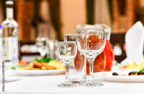 details of serving tables for a banquet in a restaurant. grapes, kiwi, tangerines, deli meats, white plates and white napkins. wine glass and vodka glasses on the table. selective focus