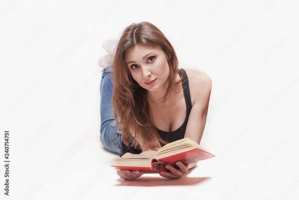 Young attractive caucasian woman lays on the floor legs up, book with red cover in the hands, slightly smile. Brown hair and eyes, wearing casual. White background, studio, isolated. Young attractive caucasian woman lays on the floor legs up, book with red cover in the hands, slightly smile. Brown hair and eyes, wearing casual. White background, studio, isolated.