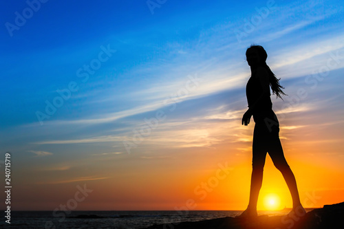 Silhouette of slim woman on the sea coast during amazing sunset.