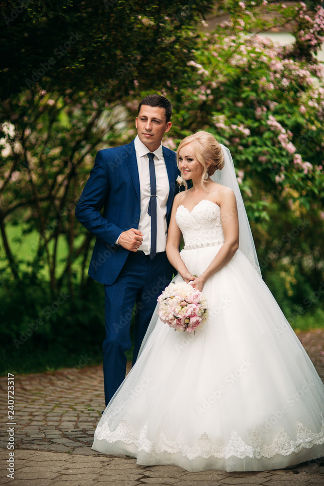 Handsome groom hug his bride in their wedding day. Background of flowering trees Handsome groom hug his bride in their wedding day. Background of flowering trees