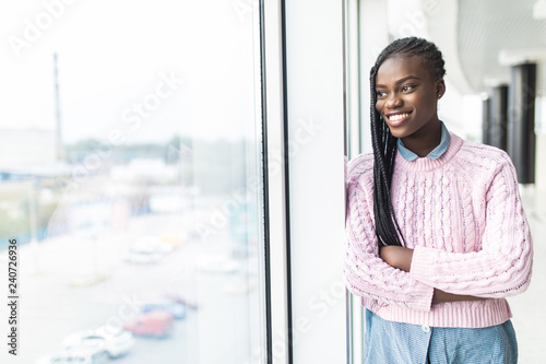 Attractive young african businesswoman staring thoughtfully through office windows at the city skyline