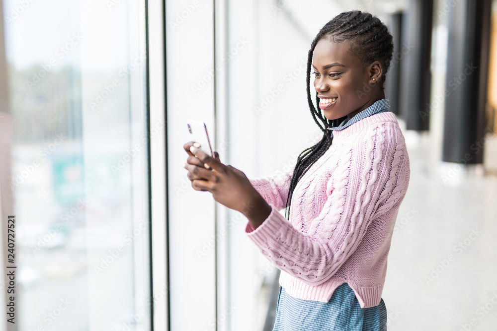 Young african woman surf in internet in mobile phone in front of panoramic windows Young african woman surf in internet in mobile phone in front of panoramic windows