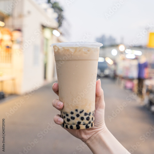 A young woman is holding a plastic cup of brown sugar bubble milk tea at a night market in Taiwan, Taiwan delicacy, close up. photo