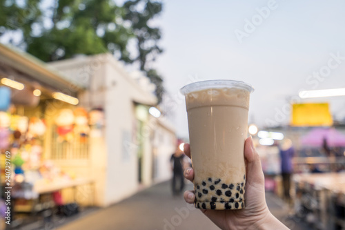 A young woman is holding a plastic cup of brown sugar bubble milk tea at a night market in Taiwan, Taiwan delicacy, close up.