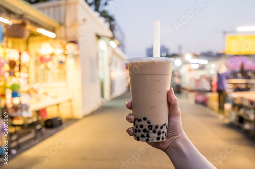 A young woman is holding a plastic cup of bubble milk tea with a straw at a night market in Taiwan  Taiwan delicacy  close up.