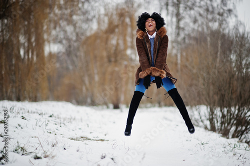 Curly hair african american woman wear on sheepskin coat and gloves posed at winter day, having fun and jump.