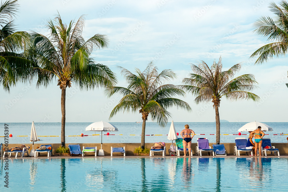 Obraz premium W godzinach porannych ludzie relaksują się między basenem a tropikalnym morzem.
