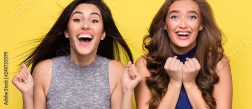 Two overjoyed women screaming in surprise on yellow background