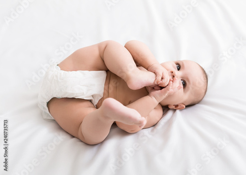 Slika na platnu Adorable little baby sucking foot lying on bed