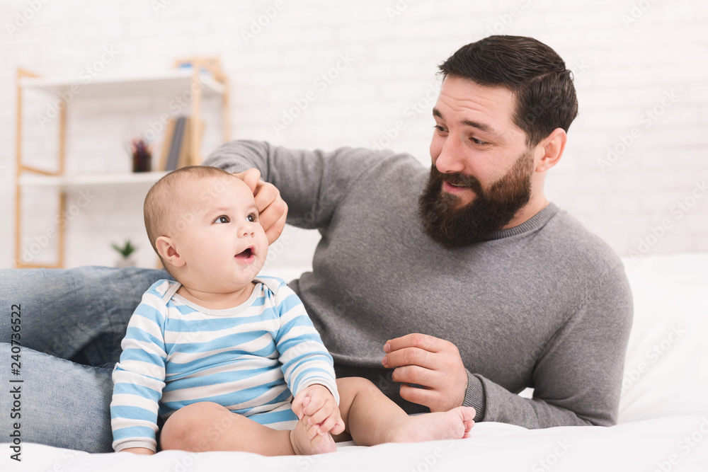 Young bearded man playing with his little baby in bed Young bearded man playing with his little baby in bed