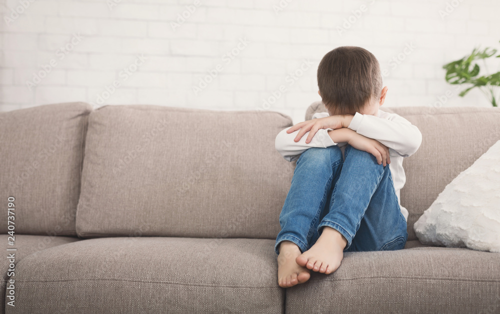 Boy hugging his knee in tear, sitting on sofa Boy hugging his knee in tear, sitting on sofa