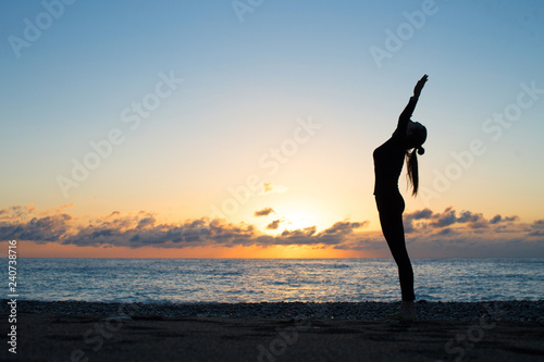 Female silhouette greeting to the rising sun on the beach in the morning