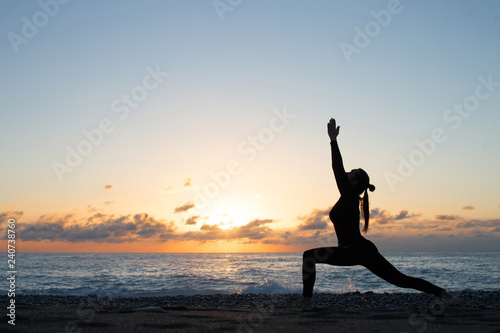 Human silhouette doing yoga on the beach in front of rising sun