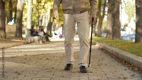 Fall, weak grandad limping slowly, carefully along parkway, leaning on old cane