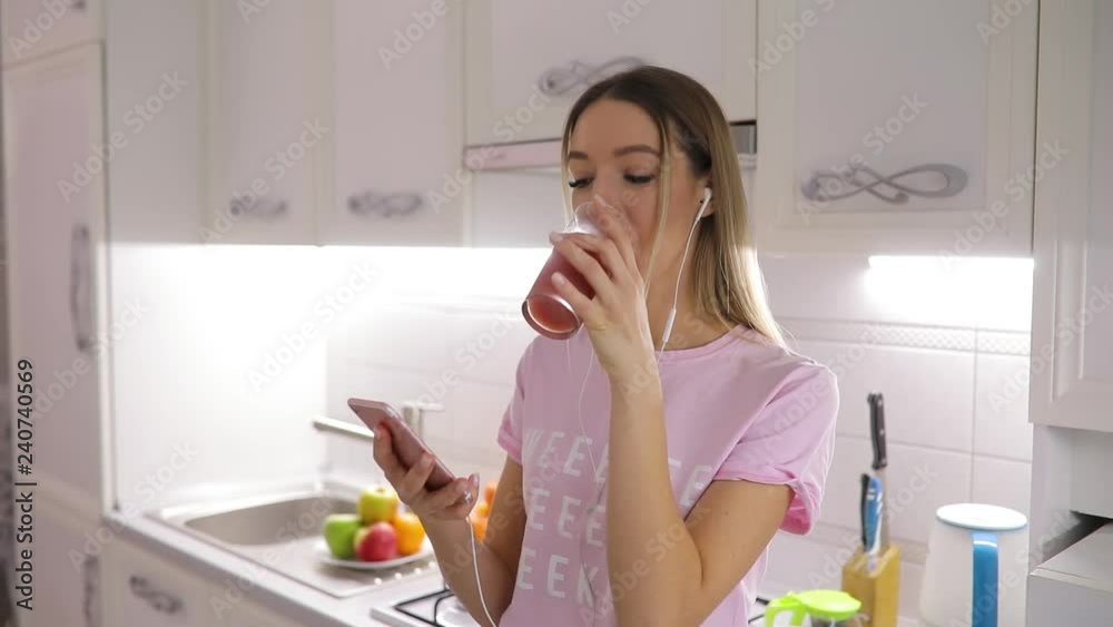 Happy morning, woman drinking juice standing on kitchen listening to music at home Happy morning, woman drinking juice standing on kitchen listening to music at home