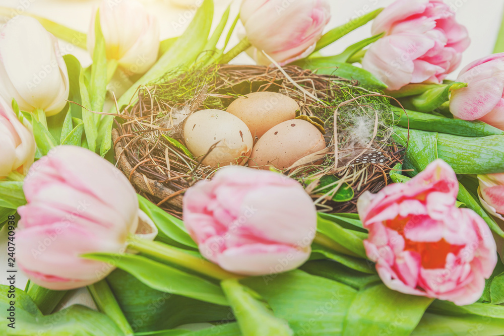 Spring greeting card. Easter eggs in nest with moss and pink fresh tulip flowers bouquet on rustic white wooden background. Easter concept. Flat lay top view copy space. Spring flowers tulips
