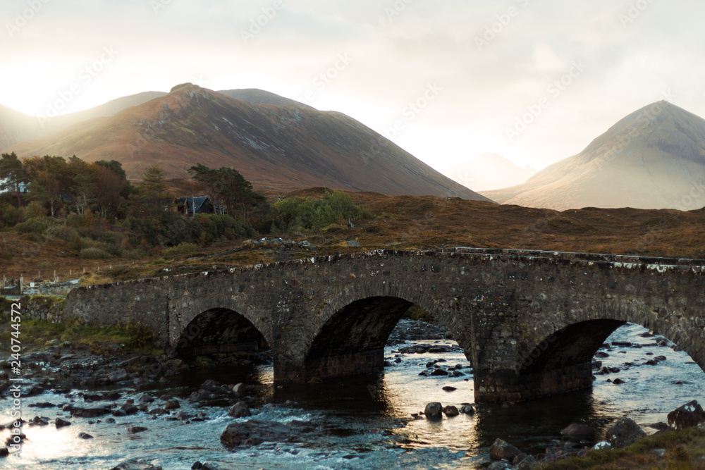 Sligachan Bridge at sunrise covered in sun rays in front of impressive mountain range (Isle of Skye, Scotland, Europe)