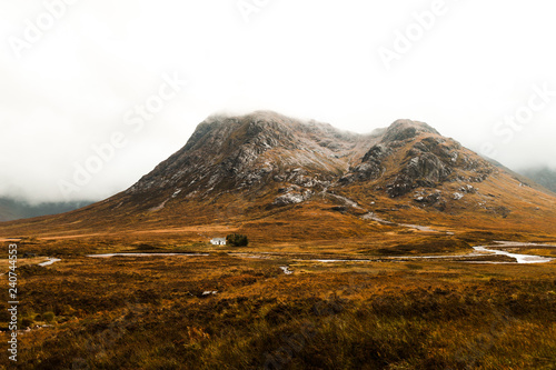 Lonely white cottage on a foggy autumn day in the valley of Glen Coe in front of impressive mountain formations (Glen Coe, Scotland, Europe)