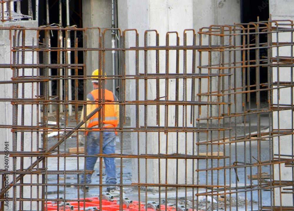 Steel frame of a reinforced concrete structure at a construction site, with the blurred image of a construction worker in the background (bokeh effect), Tirana, Albania