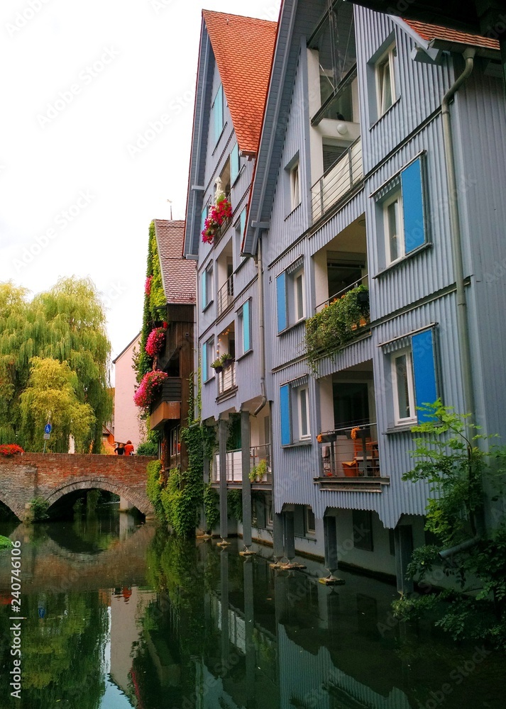 Ulm, Germany - August 23 2018: View of one of Ulm's canals at Fischerviertel, with typical architecture along the banks and two women standing on a bridge in the background