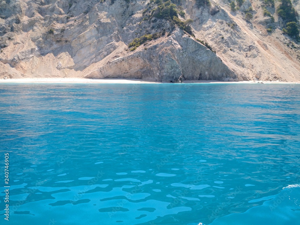 The turquoise waters of the Ionian sea around the Greek Ionian islands (Lefkada) seen from a cruise ship, with the rugged coastline and white sand beach of Egremni in the background