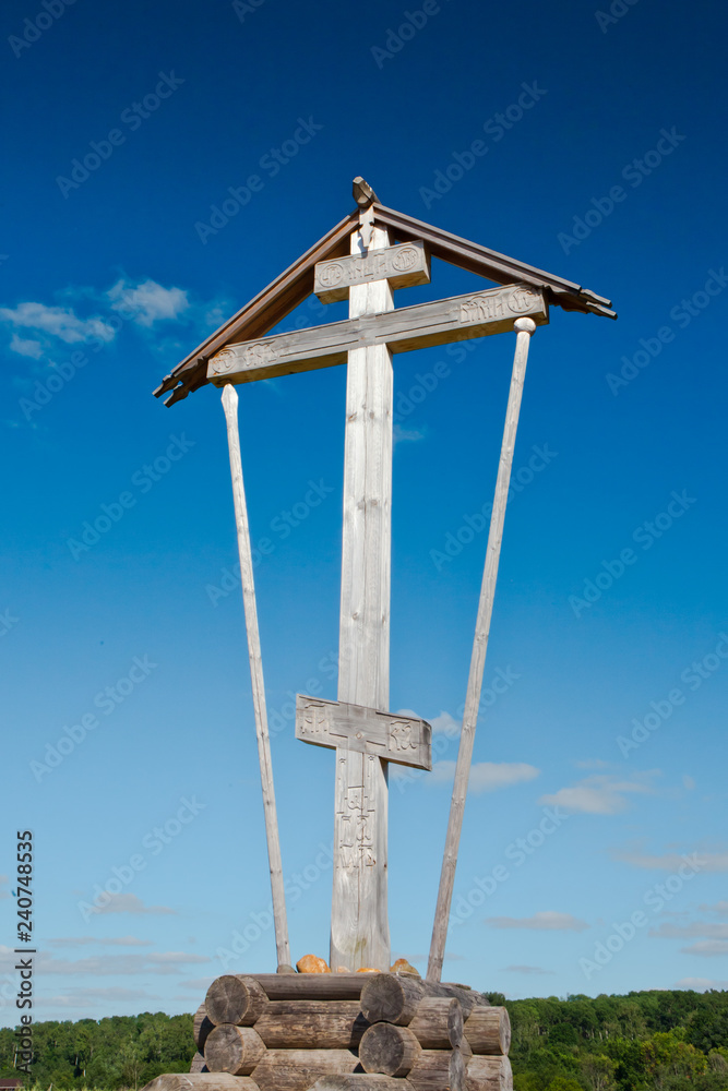 Orthodox water source Gremyachy and wooden church. Wooden monument orthodox cross on a blue sky background (not a cemetery) Orthodox water source Gremyachy and wooden church. Wooden monument orthodox cross on a blue sky background (not a cemetery)