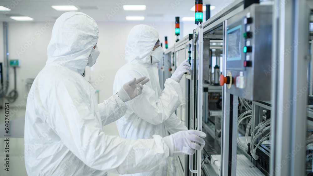Team of Scientists in Sterile Protective Clothing Work on a Modern Industrial 3D Printing Machinery. Pharmaceutical, Biotechnological and Semiconductor Creating / Manufacturing Process. Team of Scientists in Sterile Protective Clothing Work on a Modern Industrial 3D Printing Machinery. Pharmaceutical, Biotechnological and Semiconductor Creating / Manufacturing Process.