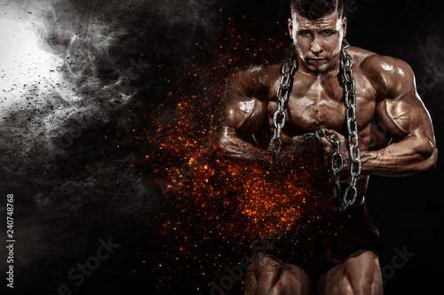 Brutal strong muscular bodybuilder athletic man pumping up muscles with chains on black background. Workout bodybuilding concept. Copy space for sport nutrition ads.